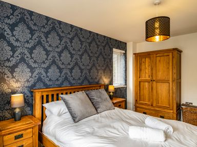 A bedroom with a wooden bed and bedside tables with lamps and a wooden wardrobe at Beach Haven in Perranporth