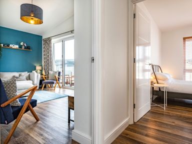 A living room with blue chairs and a beige sofa and a bedroom with a bed and side table at Beach Haven in Perranporth
