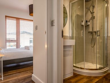 A bedroom with a bed and window blinds next to a bathroom with a shower and sink at Beach Haven in Perranporth