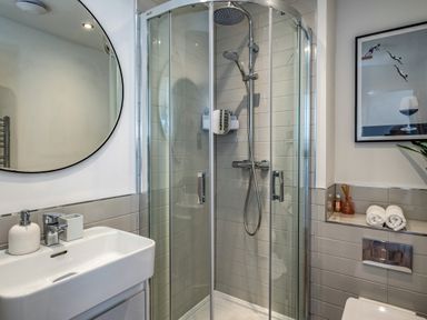 A bathroom with a glass shower enclosure a sink with a mirror and a shelf with towels and a framed picture at Beach Haven in Perranporth