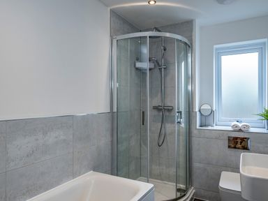 A bathroom with a corner shower cubicle bathtub toilet and window at Beach Haven in Perranporth