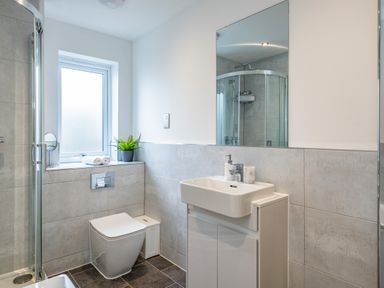 A bathroom with a sink cabinet, toilet, shower enclosure, window, and a potted plant at Beach Haven in Perranporth