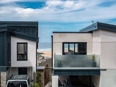A view of modern houses with balconies overlooking a beach with people and the ocean beyond at Beach Haven in Perranporth