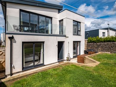 The exterior of a modern two-story house with glass balcony doors a patio area and a lawn at Beach Haven in Perranporth
