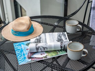A metal mesh table with two ceramic mugs a straw hat with a blue band and two magazines on it at Beach Haven in Perranporth