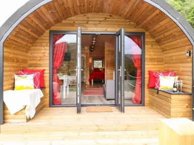A wooden pod with open glass doors showing a bed and seating area inside at Hartsop Magic - Crossgate Luxury Glamping in Hartsop near Glenridding
