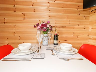 A dining table set for two with white plates bowls wine glasses flowers and a bottle of champagne in a wooden room at Hartsop Magic - Crossgate Luxury Glamping in Hartsop near Glenridding