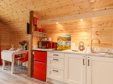 A kitchen area with white cabinets red fridge and microwave red chairs and a dining table with place settings at Hartsop Magic - Crossgate Luxury Glamping Hartsop near Glenridding