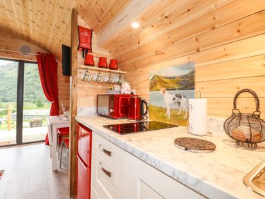 A kitchen with red appliances wooden walls a dining table and a view of green hills at Hartsop Magic - Crossgate Luxury Glamping in Hartsop near Glenridding