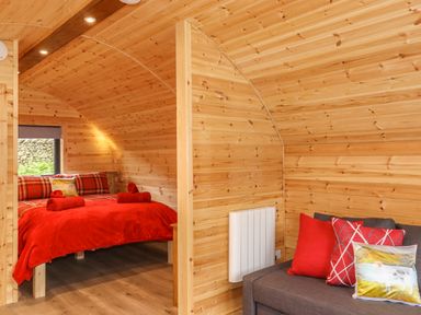 A wooden interior room with a bed and a sofa with red cushions at Hartsop Magic - Crossgate Luxury Glamping in Hartsop near Glenridding