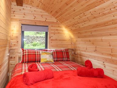 A small bedroom with a double bed red plaid bedding rolled red towels and a window showing a stone wall outside at Hartsop Magic - Crossgate Luxury Glamping in Hartsop near Glenridding