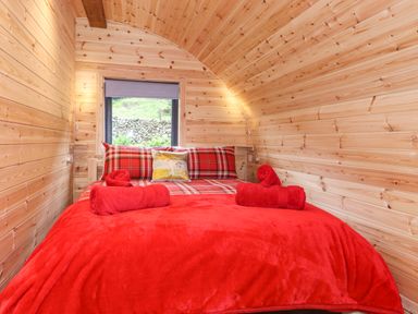 A bedroom with a double bed covered in red bedding and plaid pillows inside a wooden cabin at Hartsop Magic - Crossgate Luxury Glamping in Hartsop near Glenridding