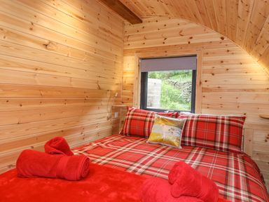 A bedroom with a red plaid bedspread and rolled red towels on the bed and wooden walls at Hartsop Magic - Crossgate Luxury Glamping Hartsop near Glenridding