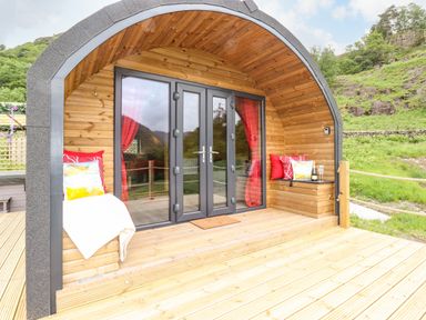 An outdoor wooden pod with glass doors red curtains and seating with cushions at Hartsop Magic - Crossgate Luxury Glamping in Hartsop near Glenridding