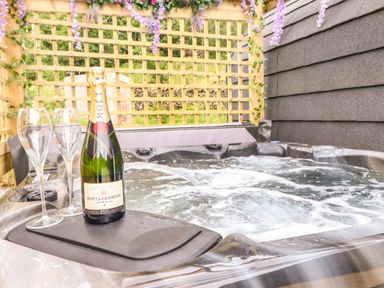 A hot tub with bubbling water a bottle of champagne and two champagne glasses under a wooden trellis with flowers at Hartsop Magic - Crossgate Luxury Glamping Hartsop near Glenridding