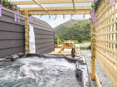 An outdoor hot tub with bubbling water under a wooden pergola with purple flowers and a picnic table in the background at Hartsop Magic - Crossgate Luxury Glamping in Hartsop near Glenridding
