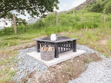 An outdoor fire pit with a basket of firewood and a jar of marshmallows on top at Hartsop Magic - Crossgate Luxury Glamping in Hartsop near Glenridding