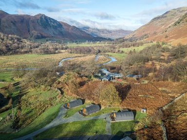 Three curved roof cabins on grassy land with winding river and hills in the background at Hartsop Magic - Crossgate Luxury Glamping in Hartsop near Glenridding