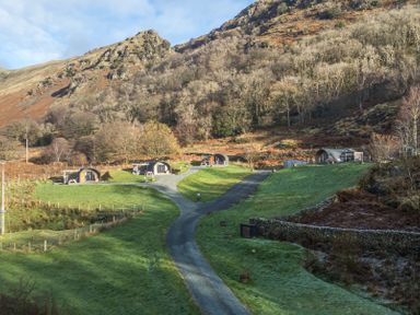 Wooden camping pods on grassy hills with gravel paths and rocky mountains in the background at Hartsop Magic - Crossgate Luxury Glamping in Hartsop near Glenridding