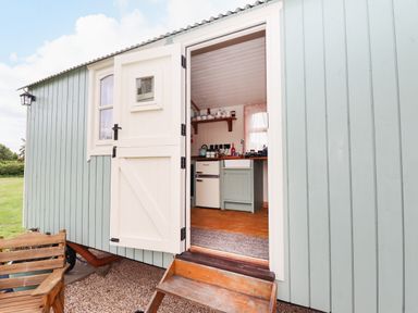 A wooden exterior door open to show a small kitchen with a fridge kettle and sink at Honeybee Lodge in Stixwould near Woodhall Spa