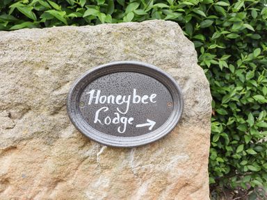 A black oval sign with Honeybee Lodge written on it attached to a large stone with green bushes behind at Honeybee Lodge in Stixwould near Woodhall Spa