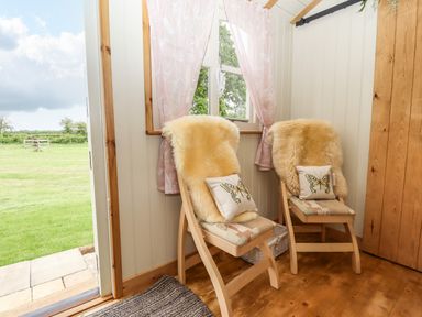 Two wooden chairs with cushions and fur throws near a window and an open door showing a grassy field at Honeybee Lodge in Stixwould near Woodhall Spa