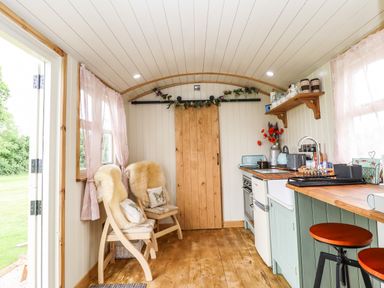 A small kitchen with wooden floor two chairs with cushions and fur covers and a sliding wooden door at Honeybee Lodge in Stixwould near Woodhall Spa