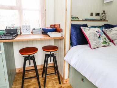 A corner with two wooden stools under a wooden counter next to a bed with patterned cushions at Honeybee Lodge in Stixwould near Woodhall Spa