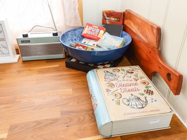 A wooden tabletop with a retro radio clock a blue bowl with card games and a cookbook shaped container at Honeybee Lodge in Stixwould near Woodhall Spa