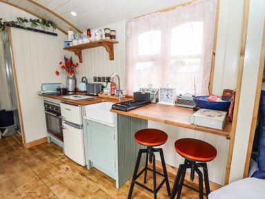 A kitchen area with wooden countertop stools a sink a small fridge an oven and various kitchen items on the counter at Honeybee Lodge in Stixwould near Woodhall Spa