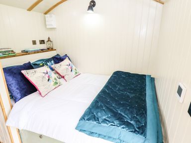 A small bedroom with a bed with pillows and a blanket and a small shelf with books and a lantern at Honeybee Lodge in Stixwould near Woodhall Spa