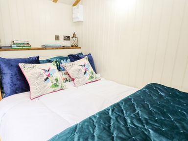A bed with pillows and a teal quilt in a room with cream paneled walls at Honeybee Lodge in Stixwould near Woodhall Spa