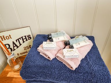 Blue and pink towels with soap and lotion tubes on a wooden surface with a hot baths sign at Honeybee Lodge in Stixwould near Woodhall Spa