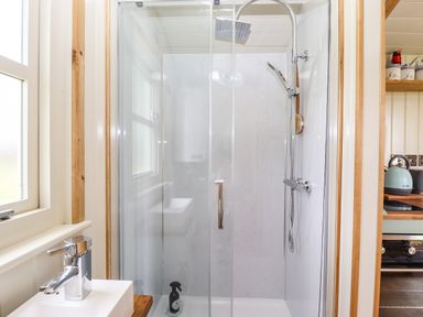 A bathroom with a glass shower enclosure a showerhead a window and a sink near a kitchen area at Honeybee Lodge in Stixwould near Woodhall Spa