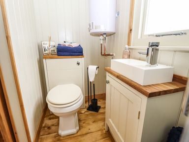 A small bathroom with a toilet a sink on a wooden cabinet towels on a storage unit and a water heater above at Honeybee Lodge in Stixwould near Woodhall Spa
