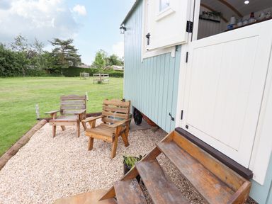 Two wooden chairs on gravel outside a small blue building with white half door and wooden steps at Honeybee Lodge in Stixwould near Woodhall Spa