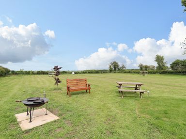 A grassy outdoor area with a fire pit a wooden bench and a picnic table at Honeybee Lodge in Stixwould near Woodhall Spa