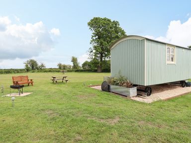 A grassy outdoor area with a light green wooden wagon on wheels a wooden bench a picnic table and a fire pit at Honeybee Lodge in Stixwould near Woodhall Spa