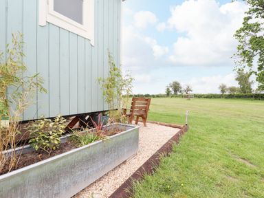 An outdoor seating area with a wooden chair and planter boxes beside a light blue building at Honeybee Lodge in Stixwould near Woodhall Spa