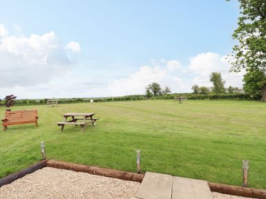A large grassy field with a wooden bench and picnic table at Honeybee Lodge in Stixwould near Woodhall Spa
