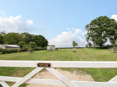 A grassy field with small trees and a wooden shed behind a white gate with a please shut the gate sign at Honeybee Lodge in Stixwould near Woodhall Spa