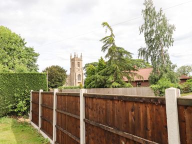 A wooden fence with trees and a church tower in the background at Honeybee Lodge in Stixwould near Woodhall Spa
