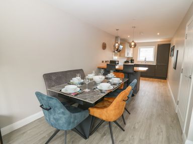 A dining table set with plates and glasses next to a kitchen with pendant lights and seating at 1 Crud Y Mor in Barmouth