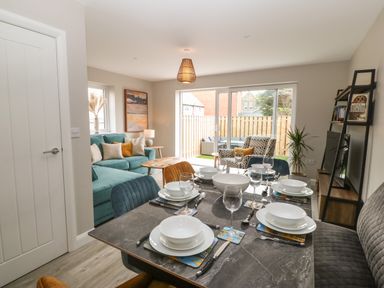 A dining table set with plates and glasses next to a living room with a turquoise sofa and an armchair at 1 Crud Y Mor in Barmouth