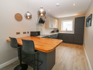 A kitchen with wooden countertop breakfast bar two stools and gray cabinets at 1 Crud Y Mor in Barmouth