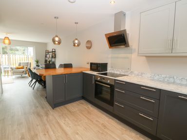 A kitchen with dark cabinets a wooden breakfast bar and dining chairs at 1 Crud Y Mor in Barmouth