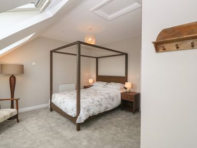 A bedroom with a four poster bed bedside tables with lamps a chair and a floor lamp at 1 Crud Y Mor in Barmouth