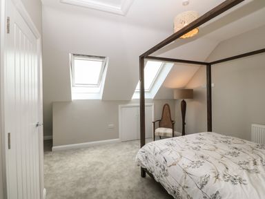 A bedroom with a canopy bed patterned bedding a chair lamp skylight windows and a closed door at 1 Crud Y Mor in Barmouth