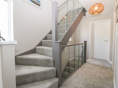 A stairway with grey carpet and glass panels a white door and a window at 1 Crud Y Mor in Barmouth