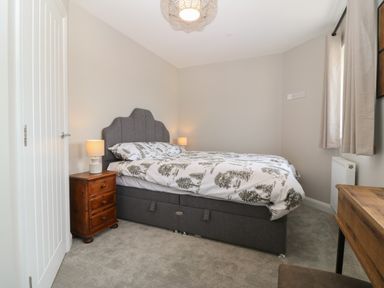 A bedroom with a grey upholstered bed and tree pattern bedding beside a wooden nightstand with lamp at 1 Crud Y Mor in Barmouth